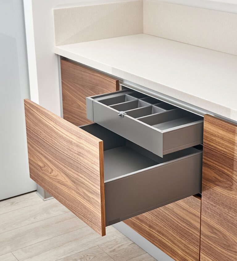 Open drawers with cutlery tray in kitchen of walnut wood with acrylic solid surface countertop